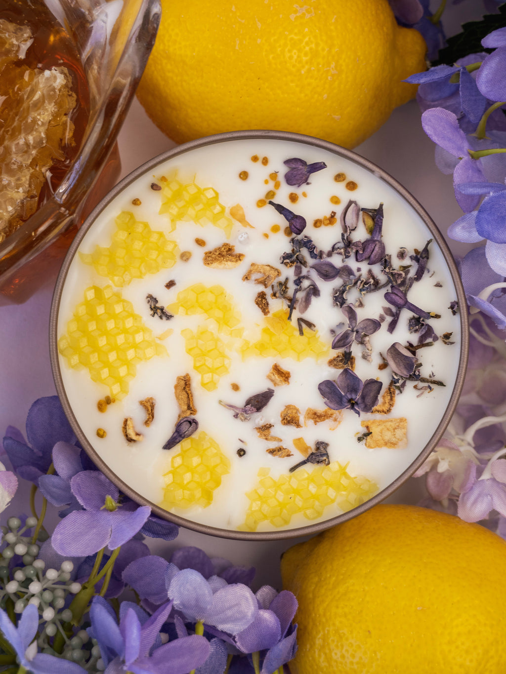 Close-up of a dessert with lemon and purple flowers, surrounded by lemons and honeycomb.