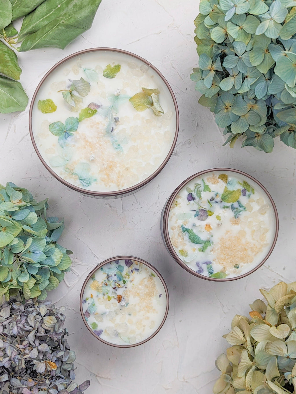 Three bowls with floral patterns on a white surface surrounded by greenery