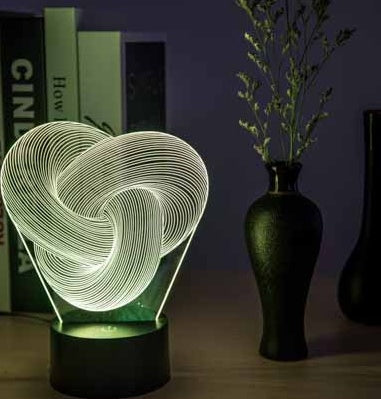 Heart-shaped 3D LED lamp on a table with books and vases in the background