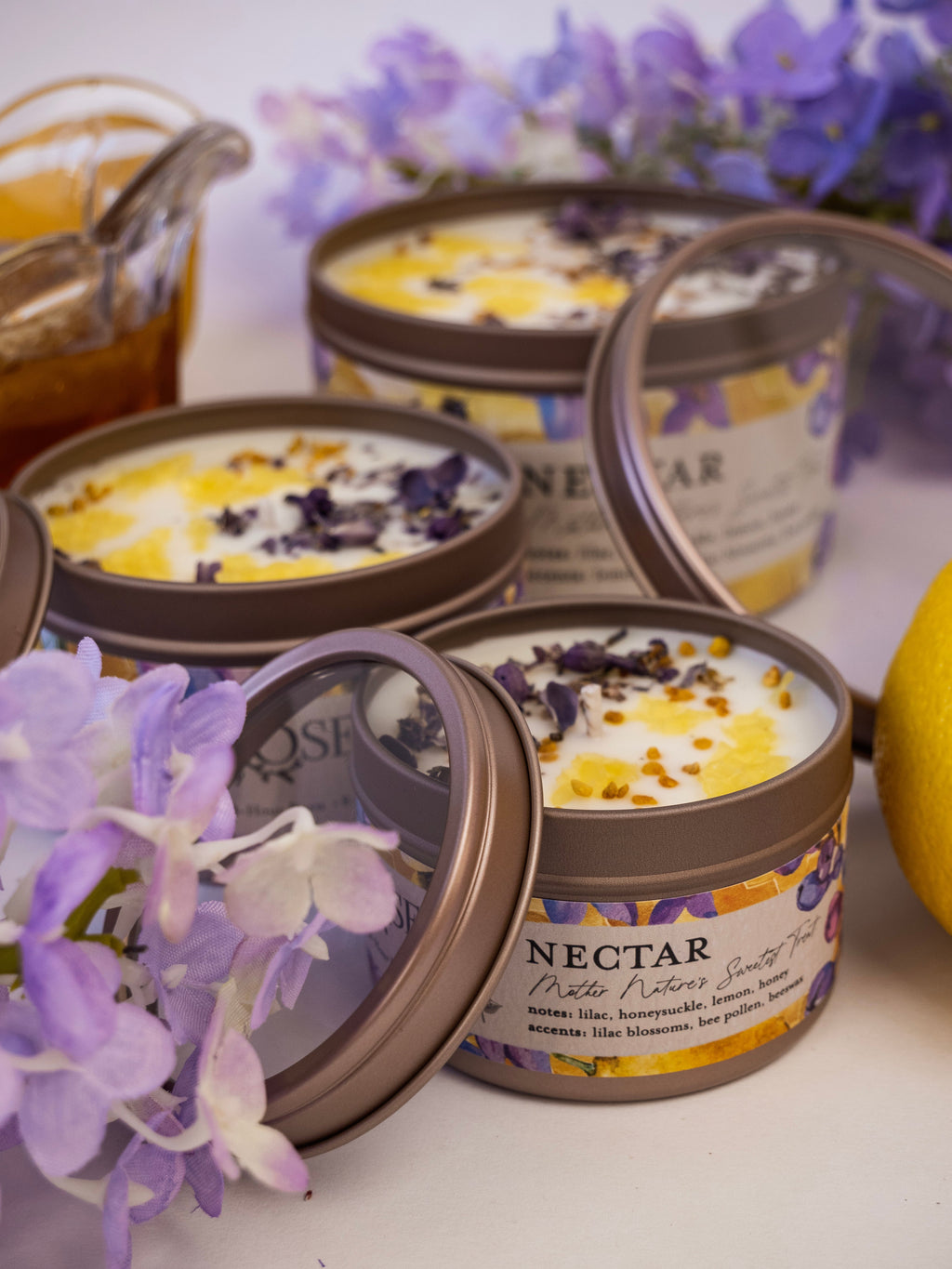 Candles in tins with 'Nectar' label surrounded by purple flowers on a white background