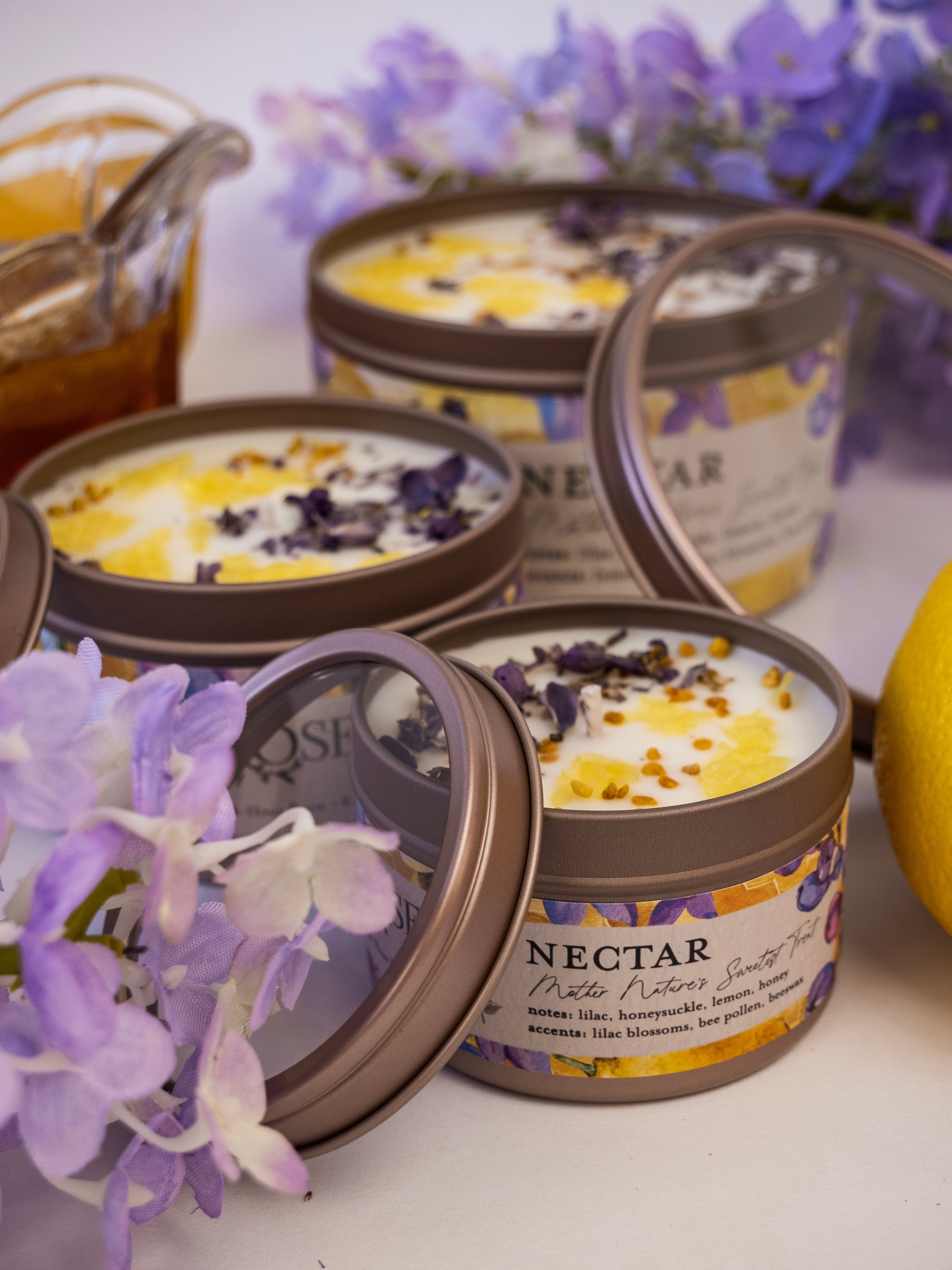 Candles in tins with 'Nectar' label surrounded by purple flowers on a white background