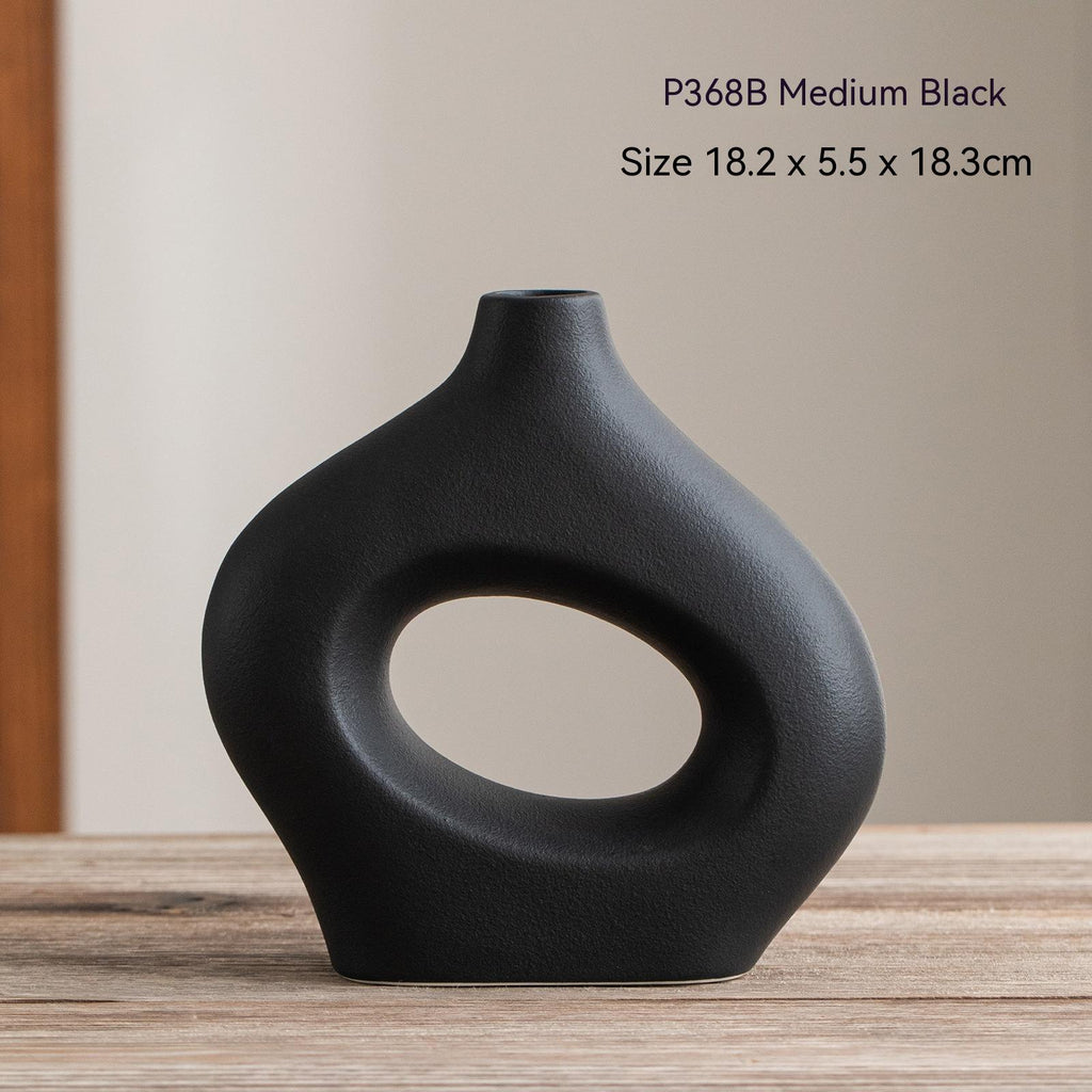 Black vase with circular design on a wooden surface and beige background