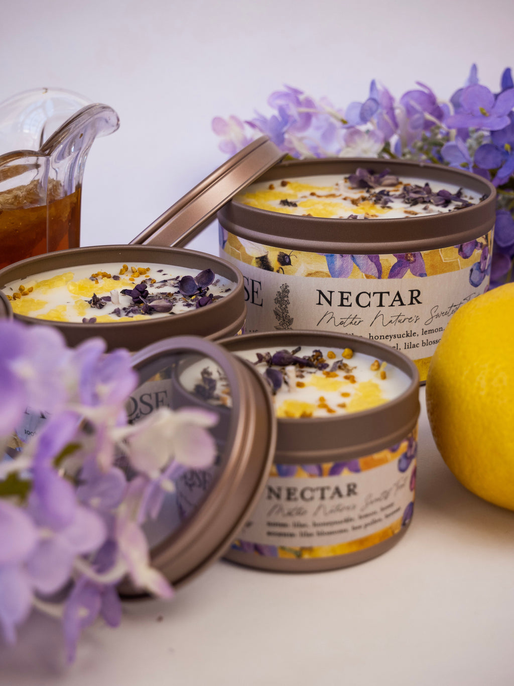 Three containers of 'Nectar' body butter with purple flowers and a lemon on a white surface.