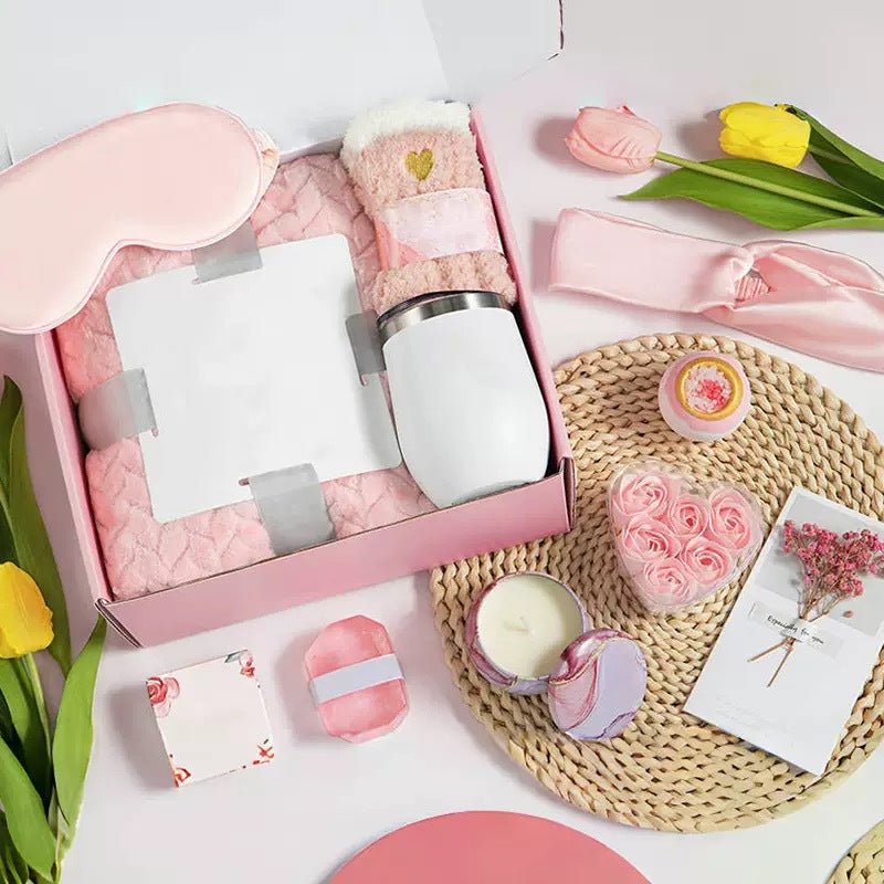 Gifting set with pink and white items including a tumbler, eye mask, and bath bombs on a white background.