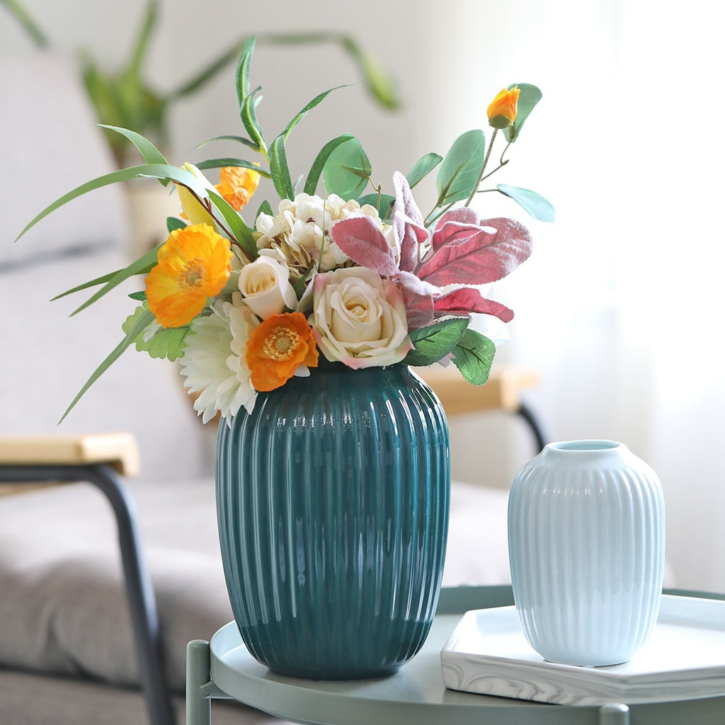 Teal vase with a floral arrangement on a table with a blurred background