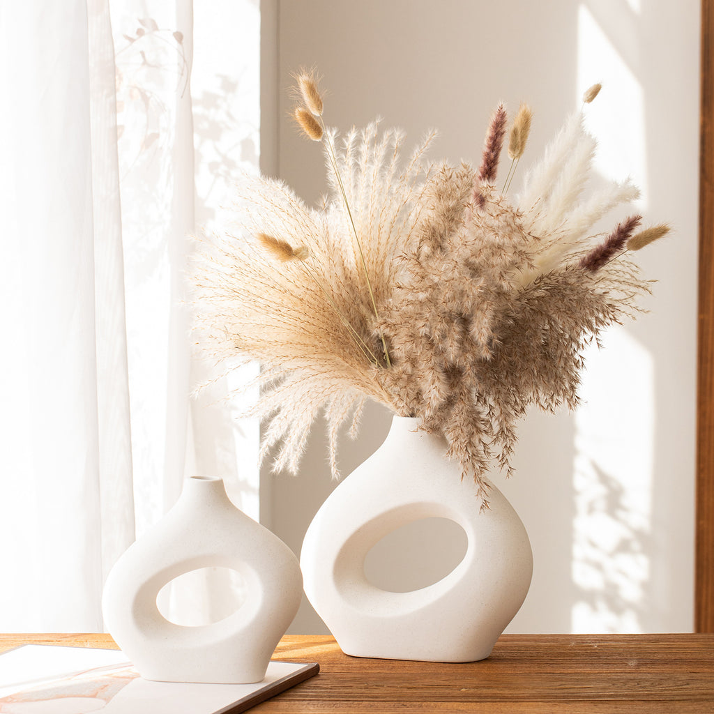 Two white abstract vases with dried pampas grass on a wooden surface.
