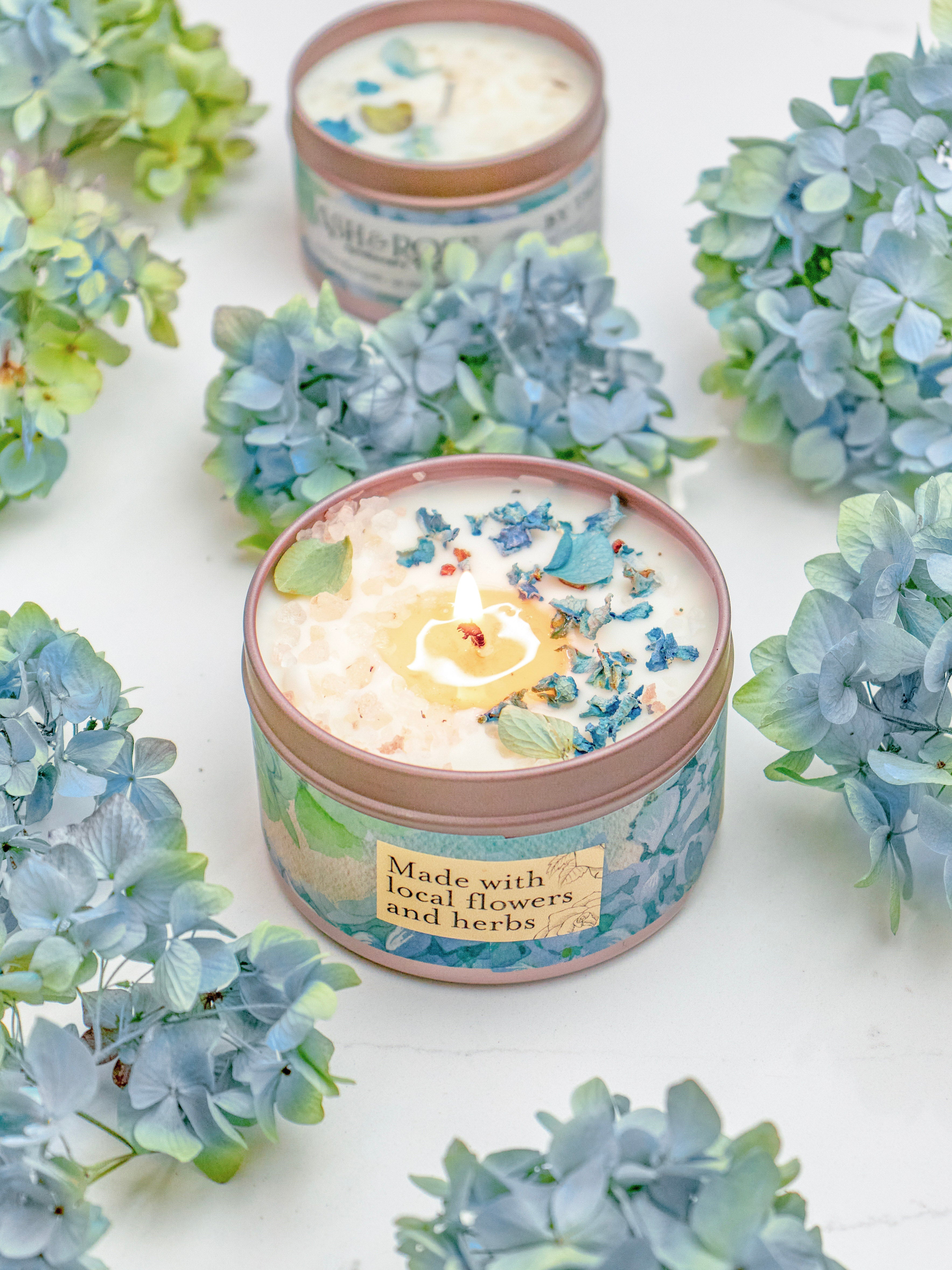 Candle in a tin surrounded by blue flowers on a white background