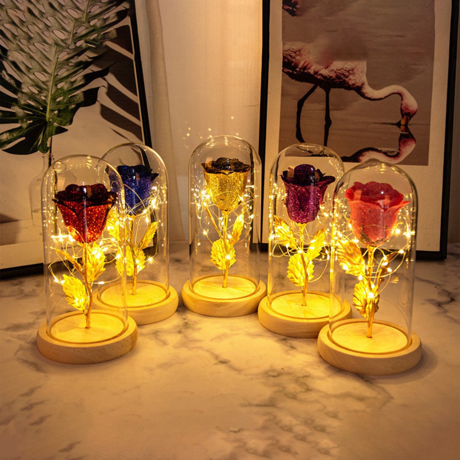 Five illuminated glass dome displays of colored roses on a marble surface.