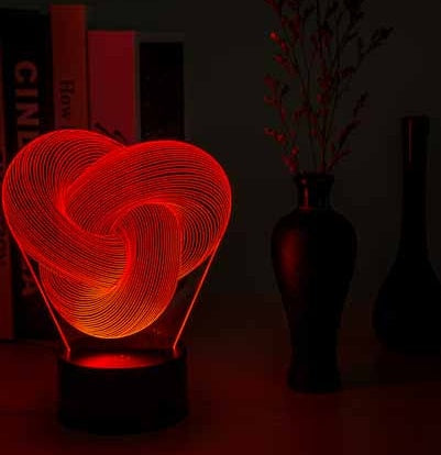Heart-shaped light fixture in a dark room with books and a vase.