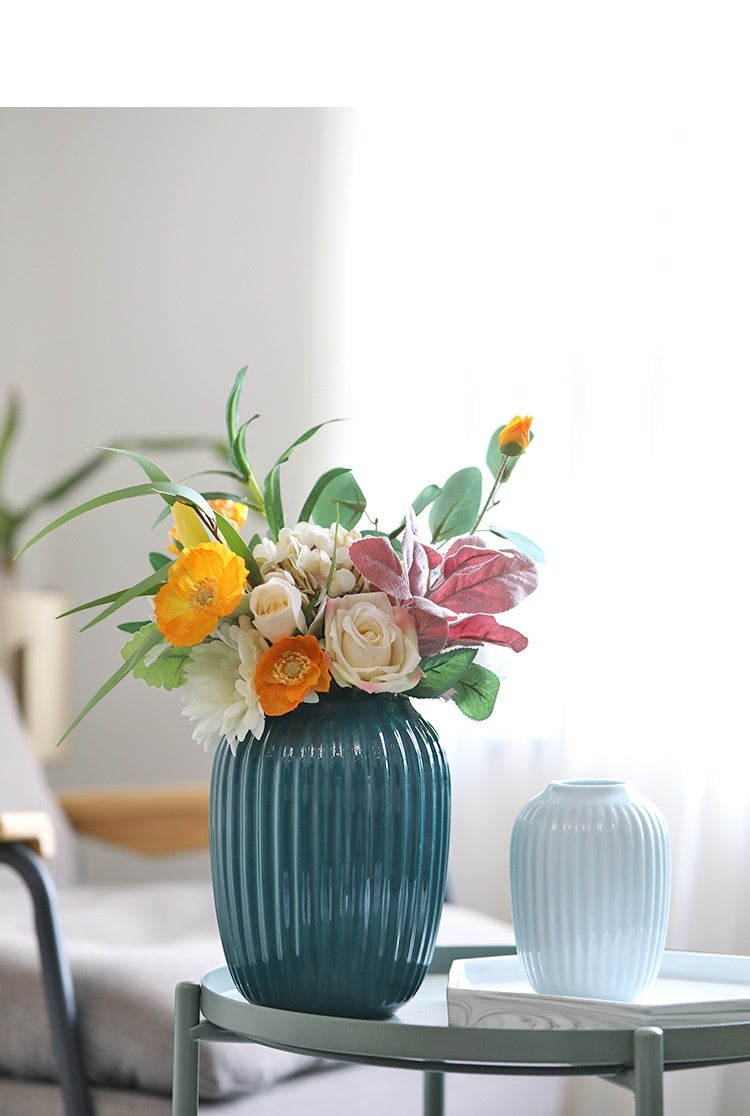 Teal vase with a floral arrangement on a table against a blurred background