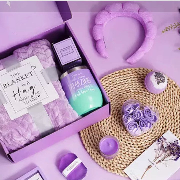 Gift set with purple and lavender items including a bottle, blanket, and headband on a pink background.