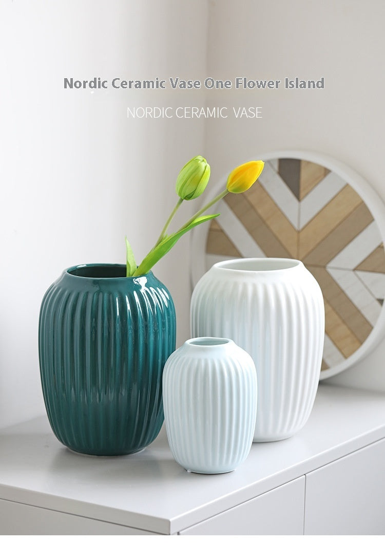 Three Nordic ceramic vases on a white surface with a decorative wall in the background.