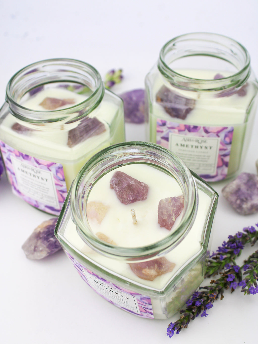 Hexagonal glass jars with candles and purple crystals on a white background