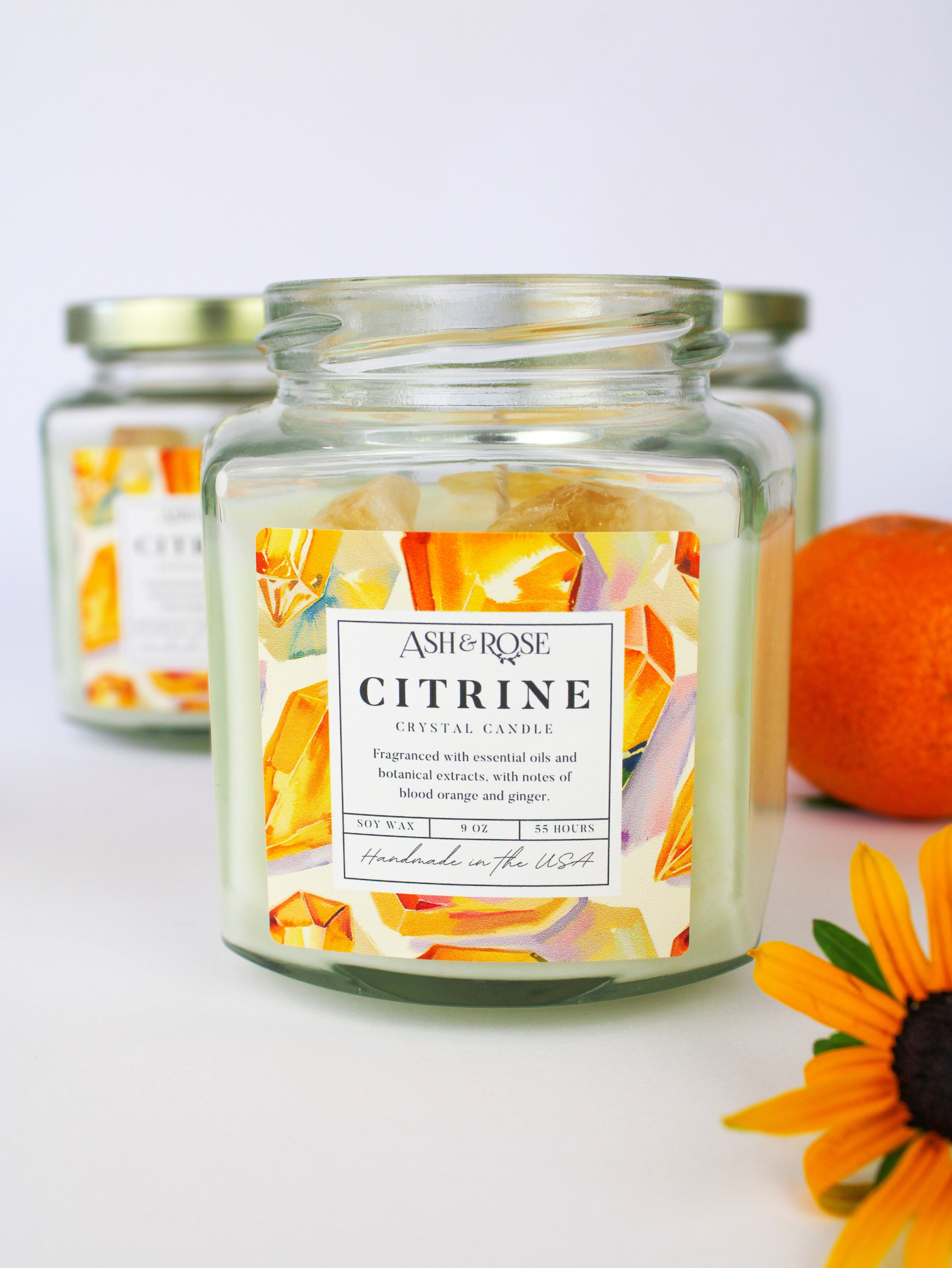 Candle jar labeled 'Citrine' by Ashleigh & Burwood with a sunflower and orange in the background.