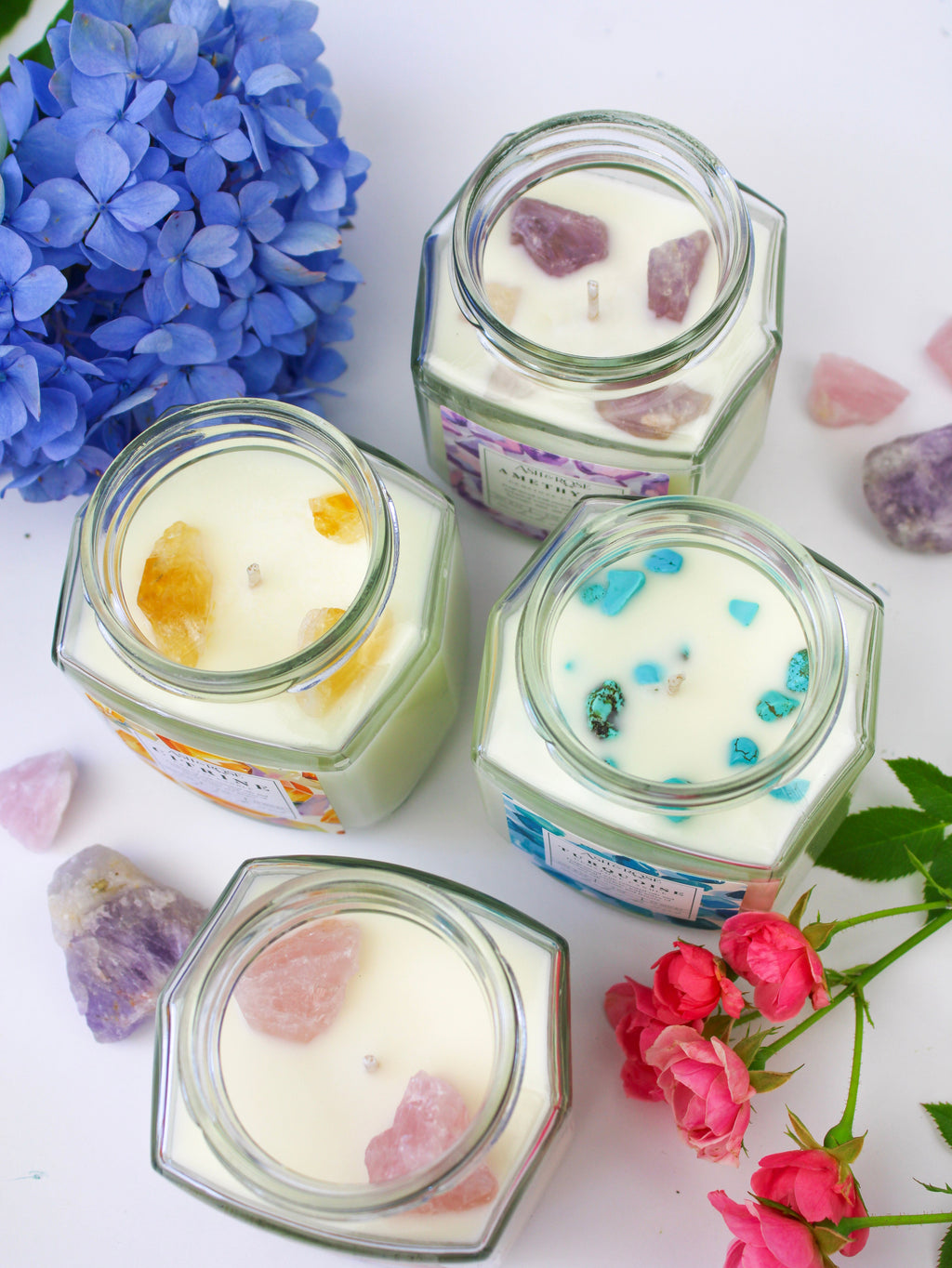 Hexagonal jars with decorative candles on a white surface with flowers.