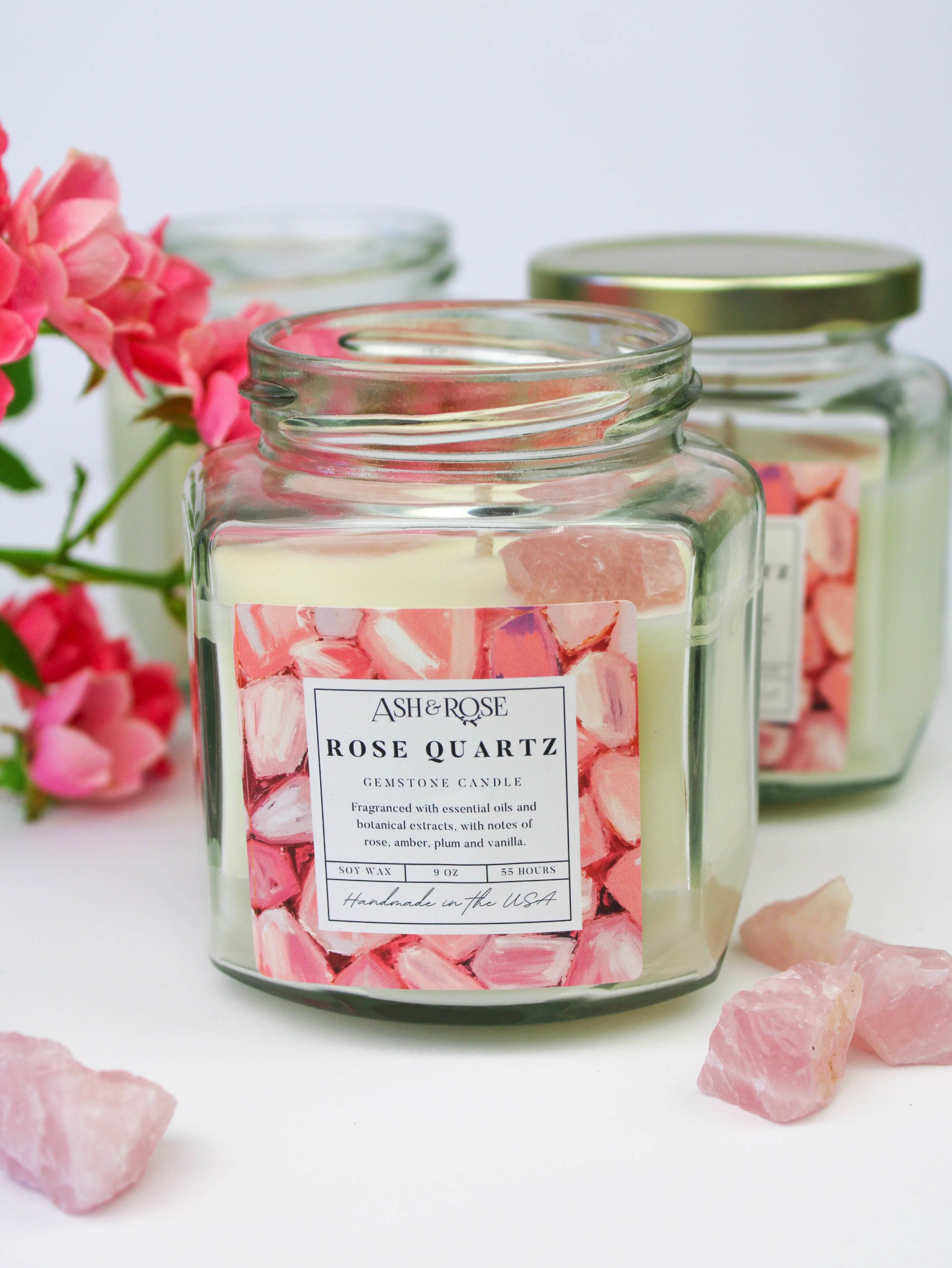 Jar candle labeled 'Rose Quartz' with pink flowers and crystals on a white background