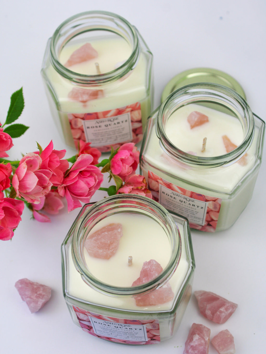 Three hexagonal glass jars with candles and pink flower petals on a white background