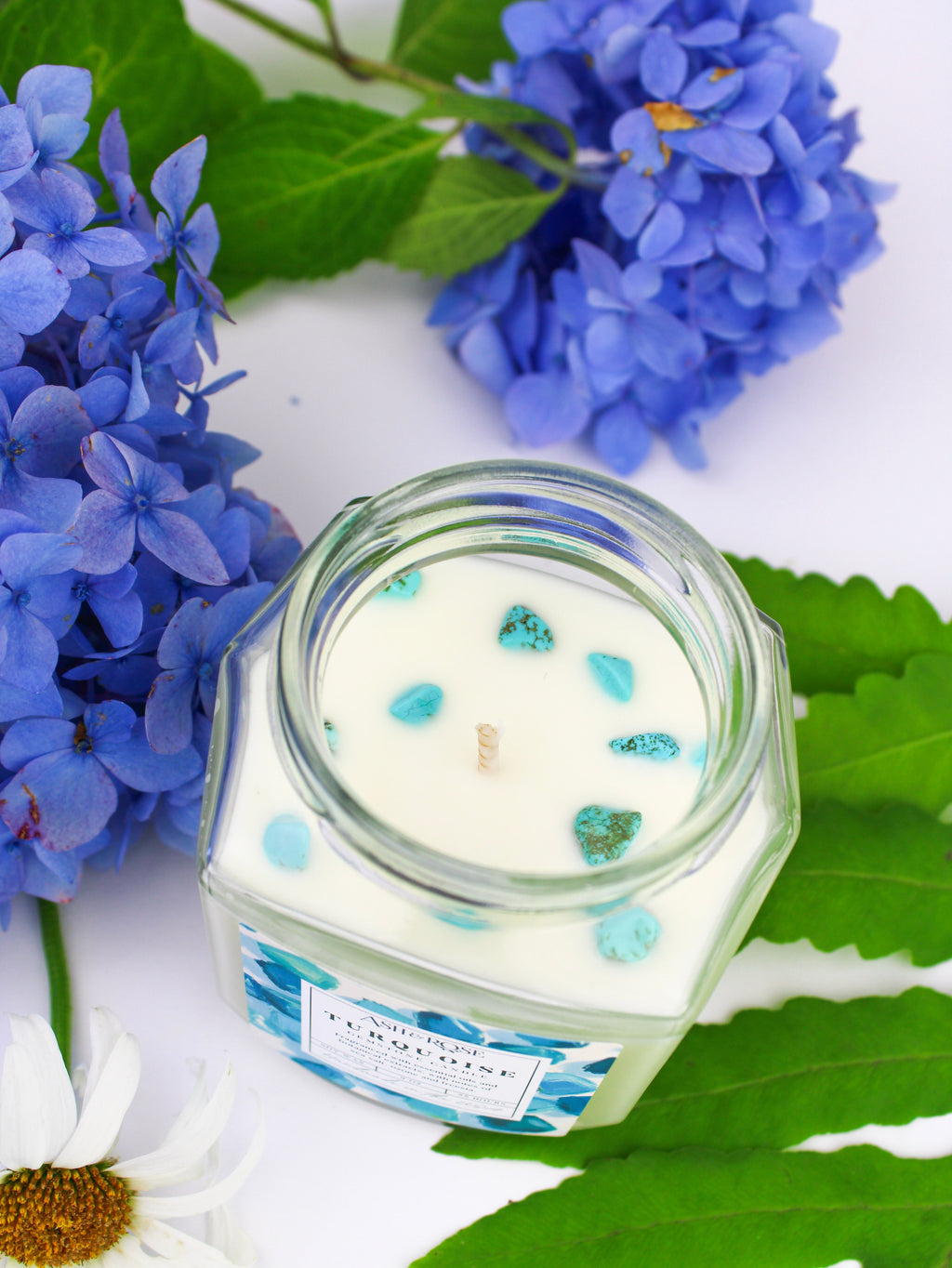 Glass candle jar with blue and green decorative elements on a white background with flowers and leaves.
