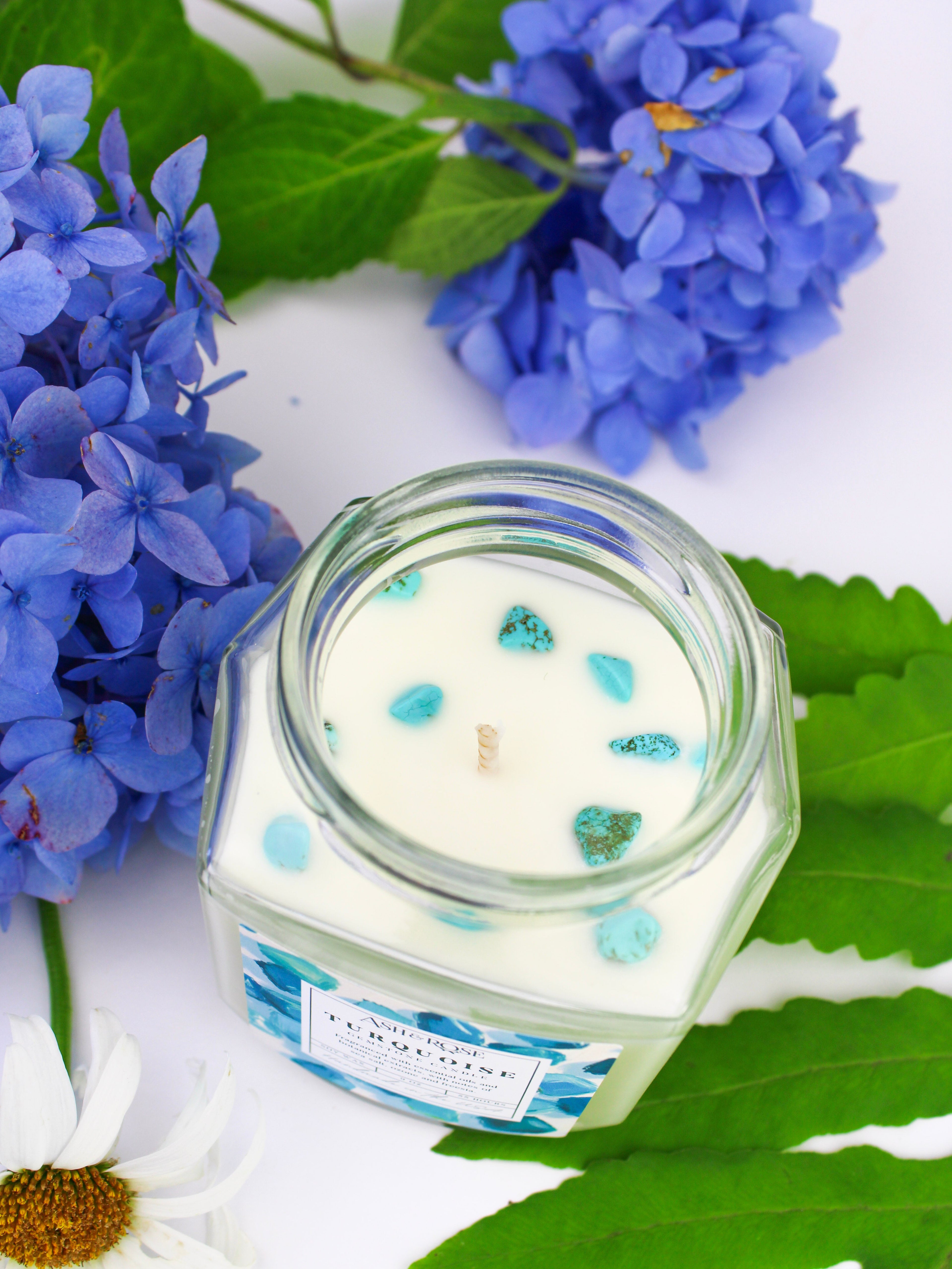 Glass candle jar with blue and green decorative elements on a white background with flowers and leaves.