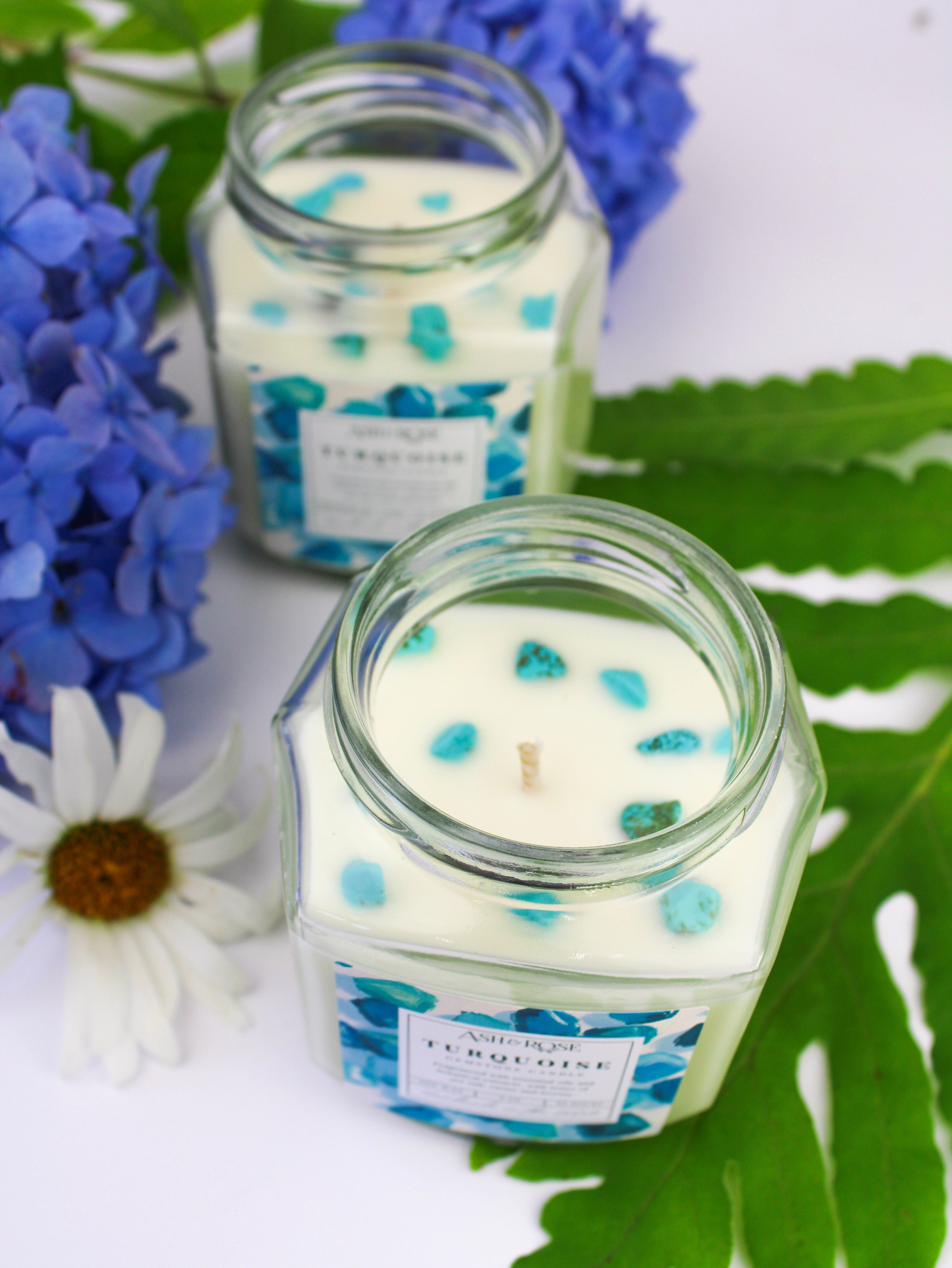 Two glass jars with candles featuring blue and green decorative elements on a white background with flowers and leaves.
