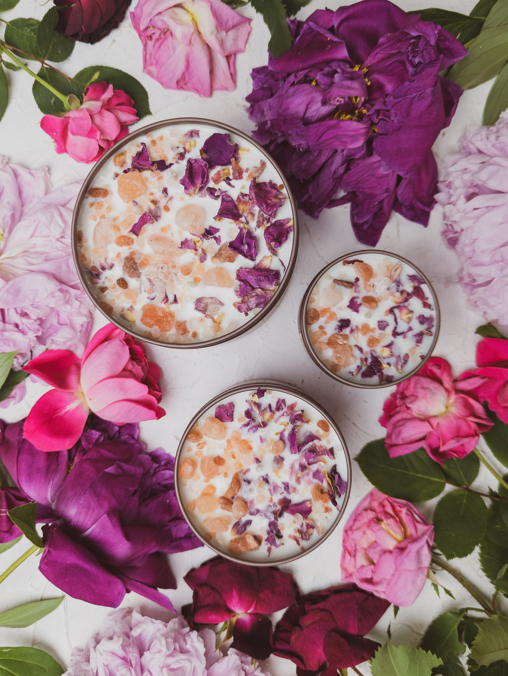 Three small containers with a floral mixture on a bed of pink and purple flowers.