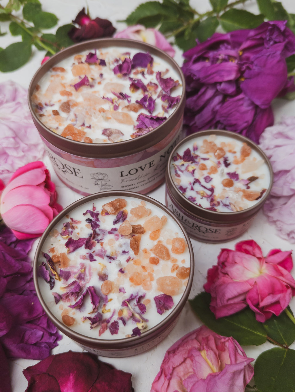 Three tins of 'Love N' Rose' body scrub with rose petals on a floral background