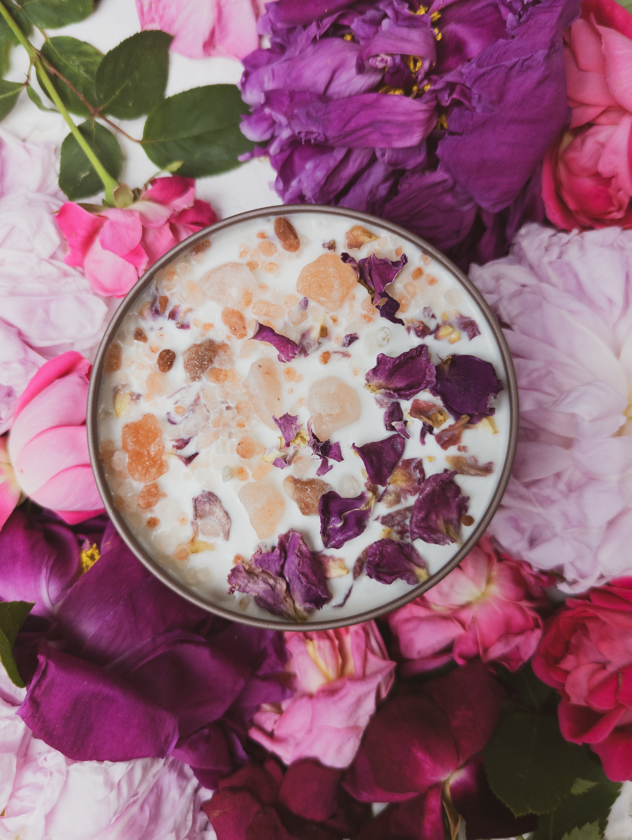 Cup of creamy dessert with rose petals on a bed of pink and purple flowers