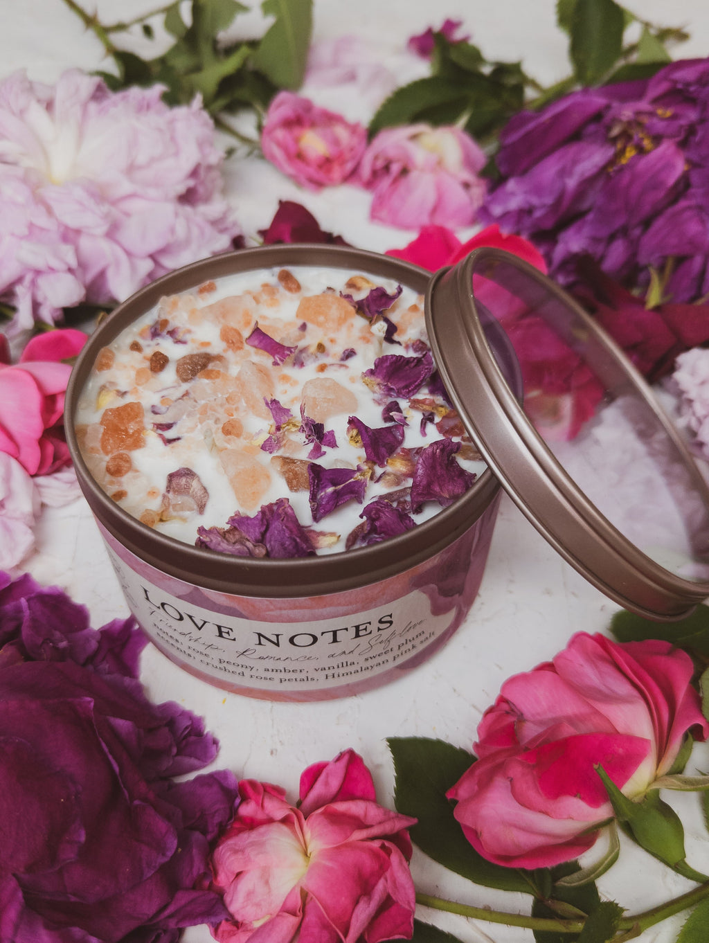 Open container of 'Love Notes' bath salts with pink and purple flowers around it
