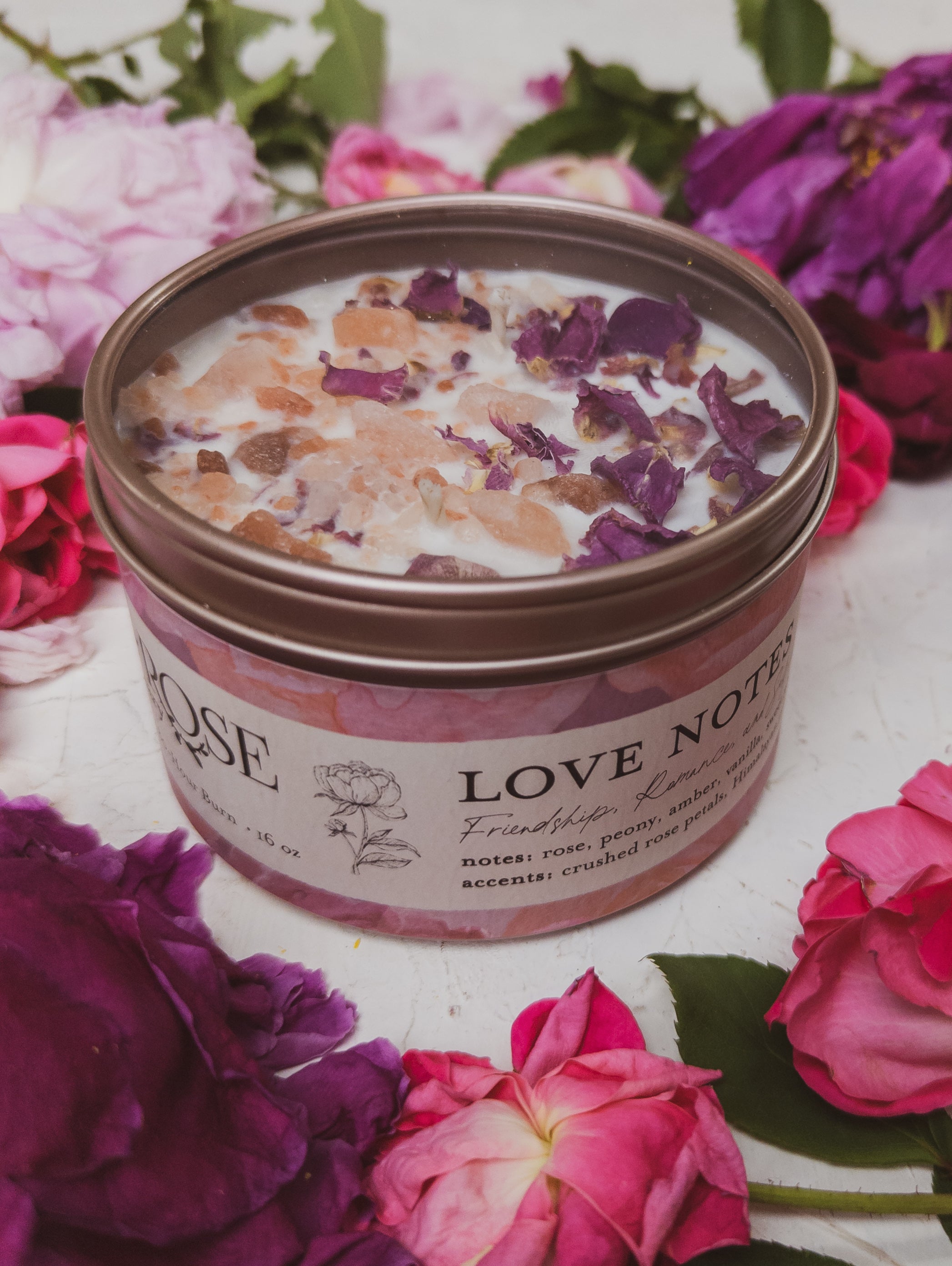 Candle in a tin labeled 'Love Notes' surrounded by pink and purple flowers
