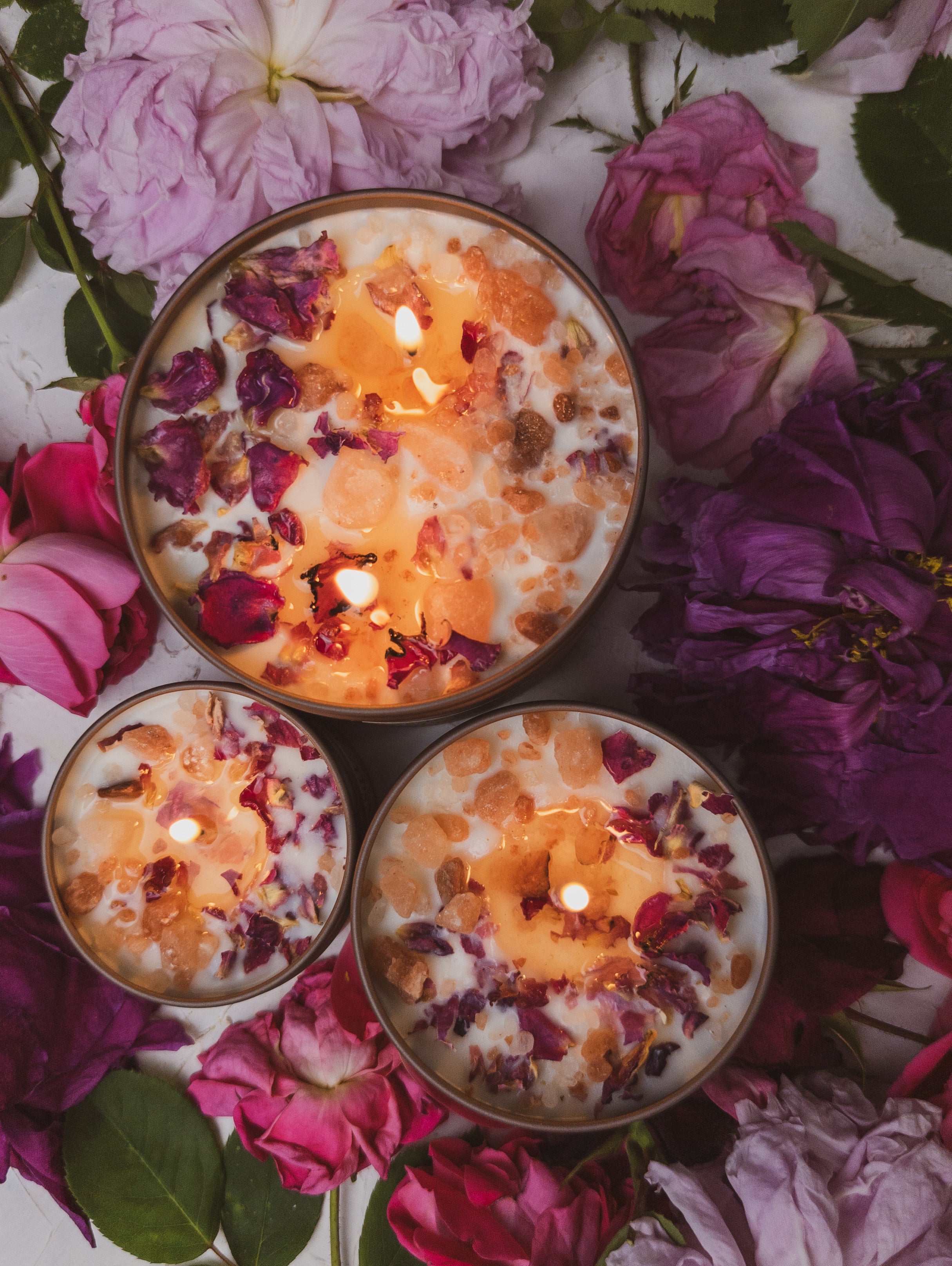Three lit candles with floral petals on a bed of pink and purple flowers