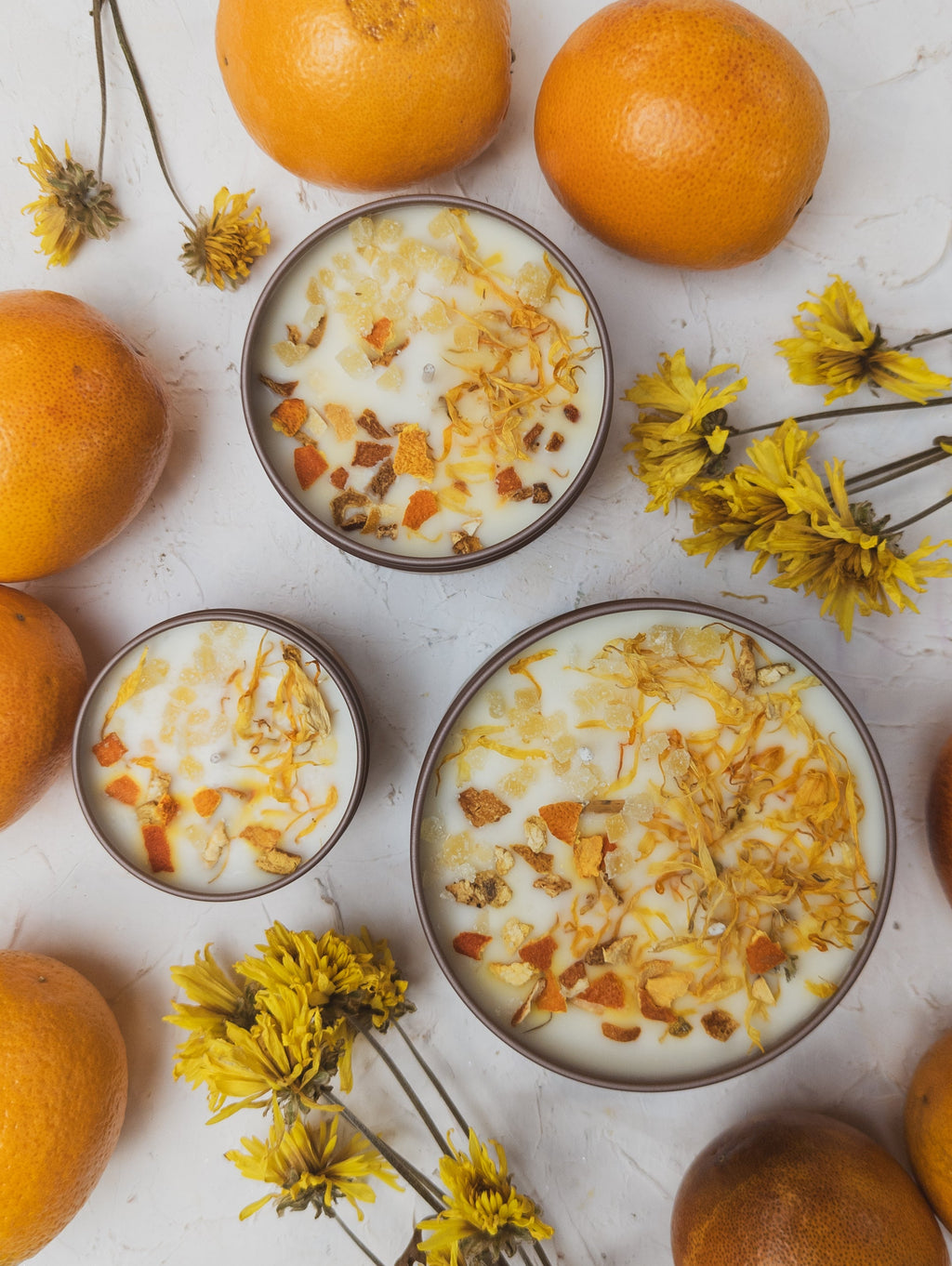 Bowls of yogurt with granola and oranges on a light surface with flowers.