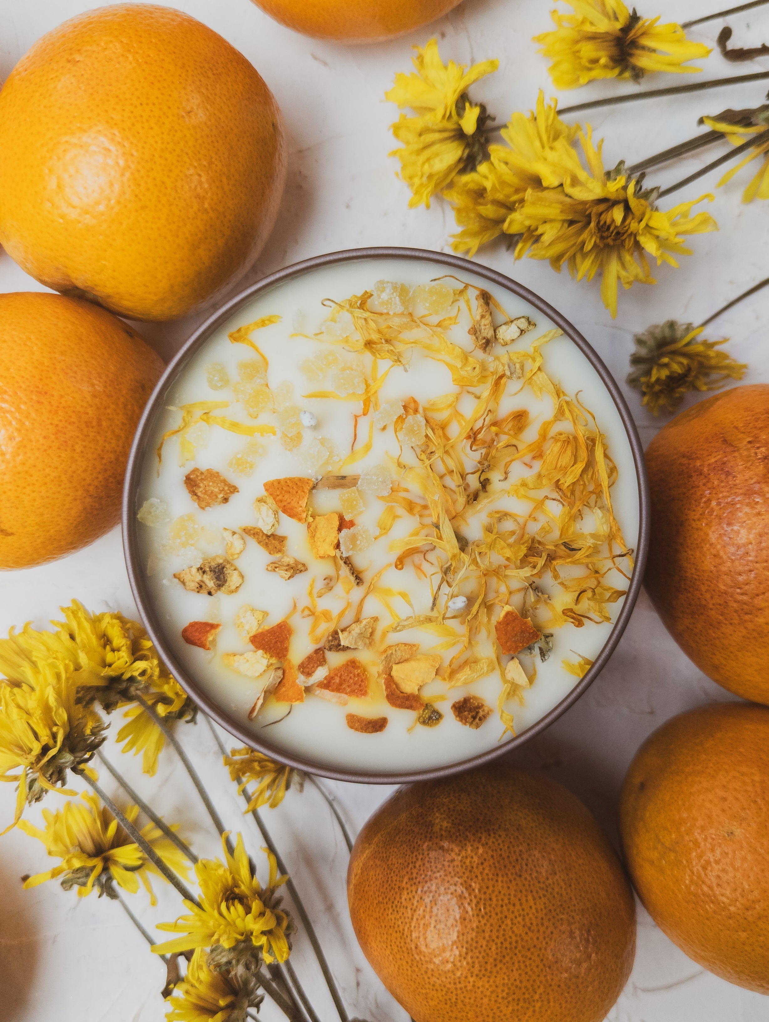 Yogurt with granola and orange pieces on a white surface with oranges and yellow flowers.