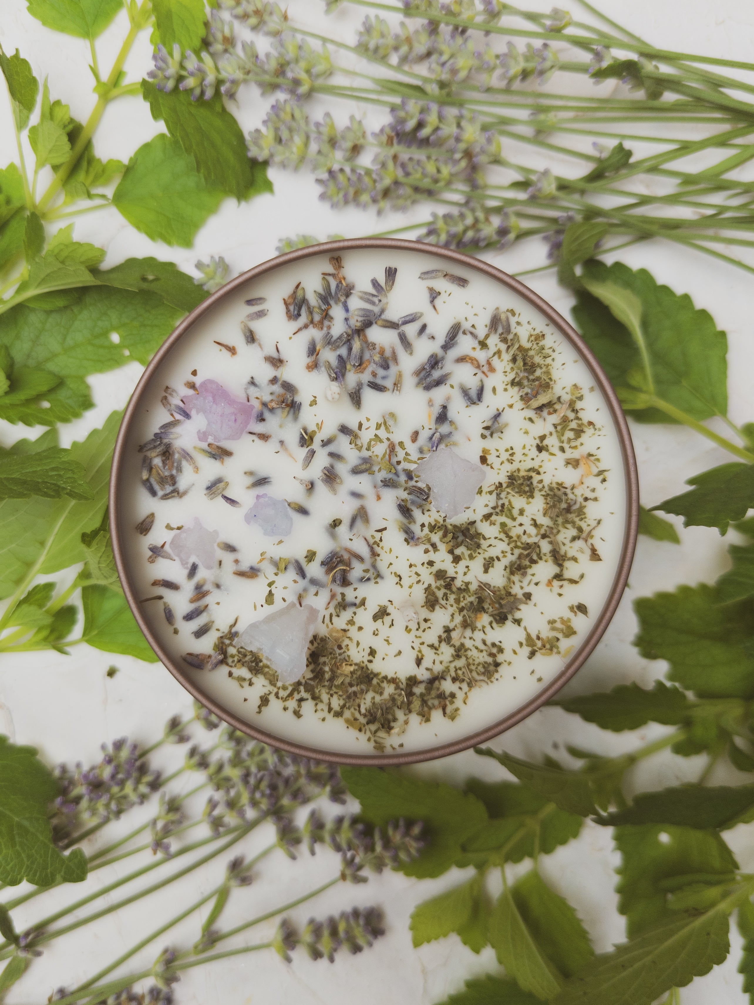 Top-down view of a bowl with dried herbs and flowers on a white background with green leaves.