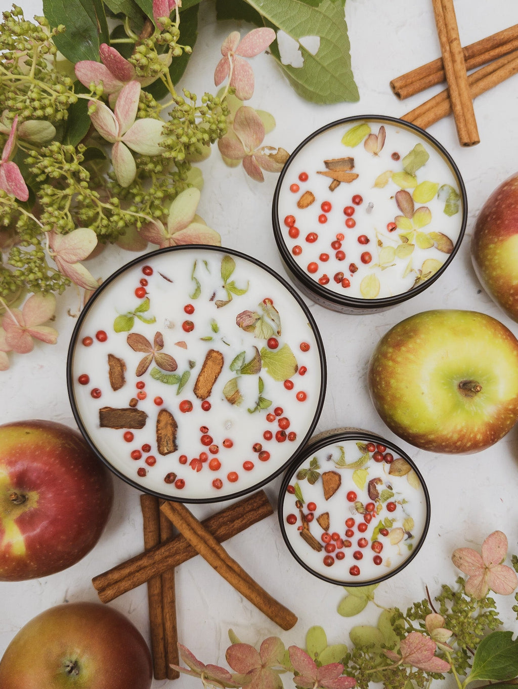 Four small dishes with a dessert topped with apples, cinnamon sticks, and decorative elements on a floral background.