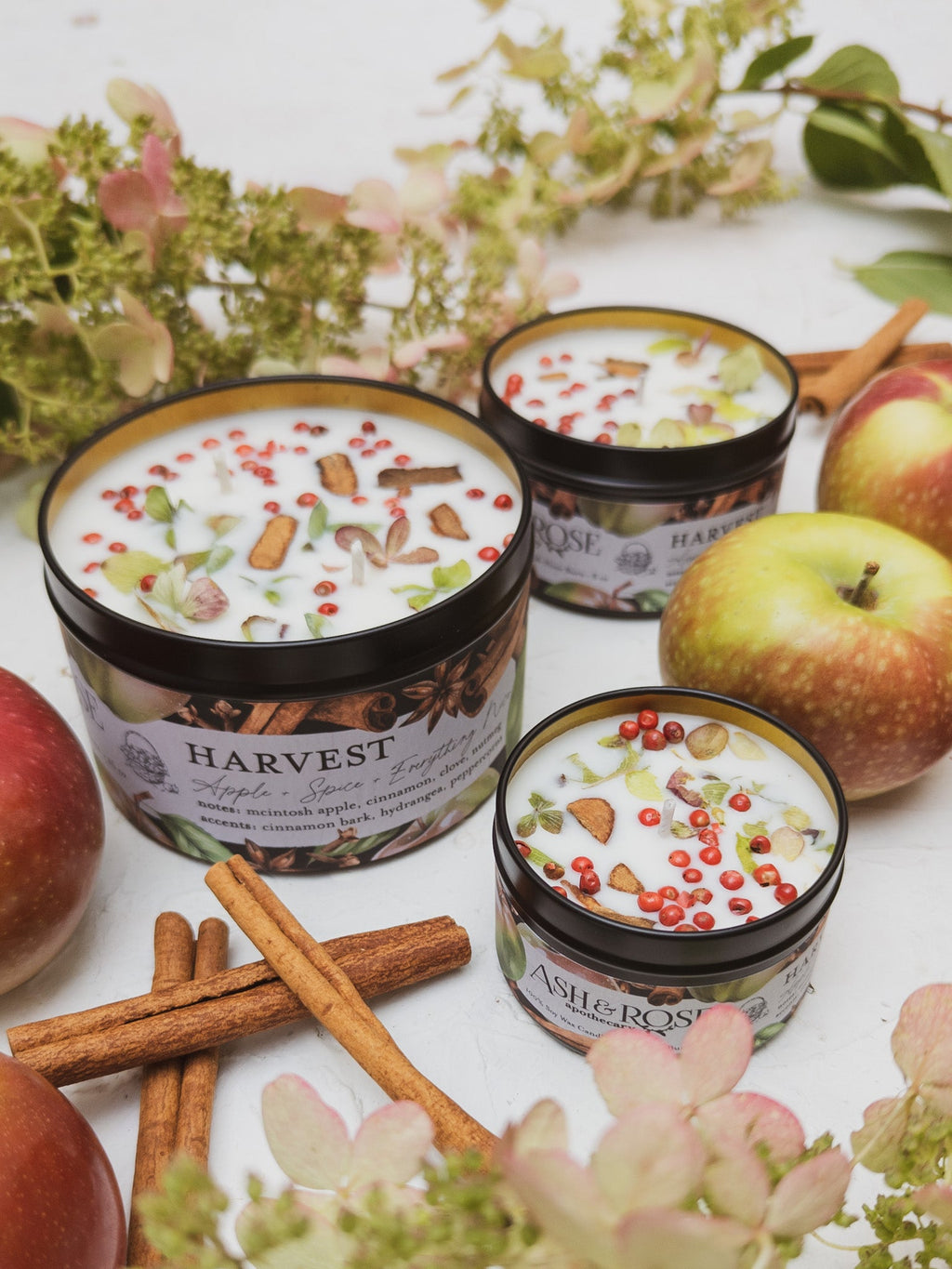 Harvest-themed candles with apples and cinnamon sticks on a white surface