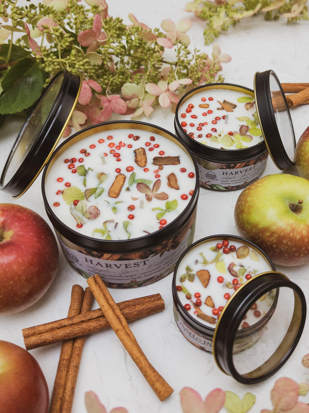 Harvest-themed candles with apples and cinnamon sticks on a white surface