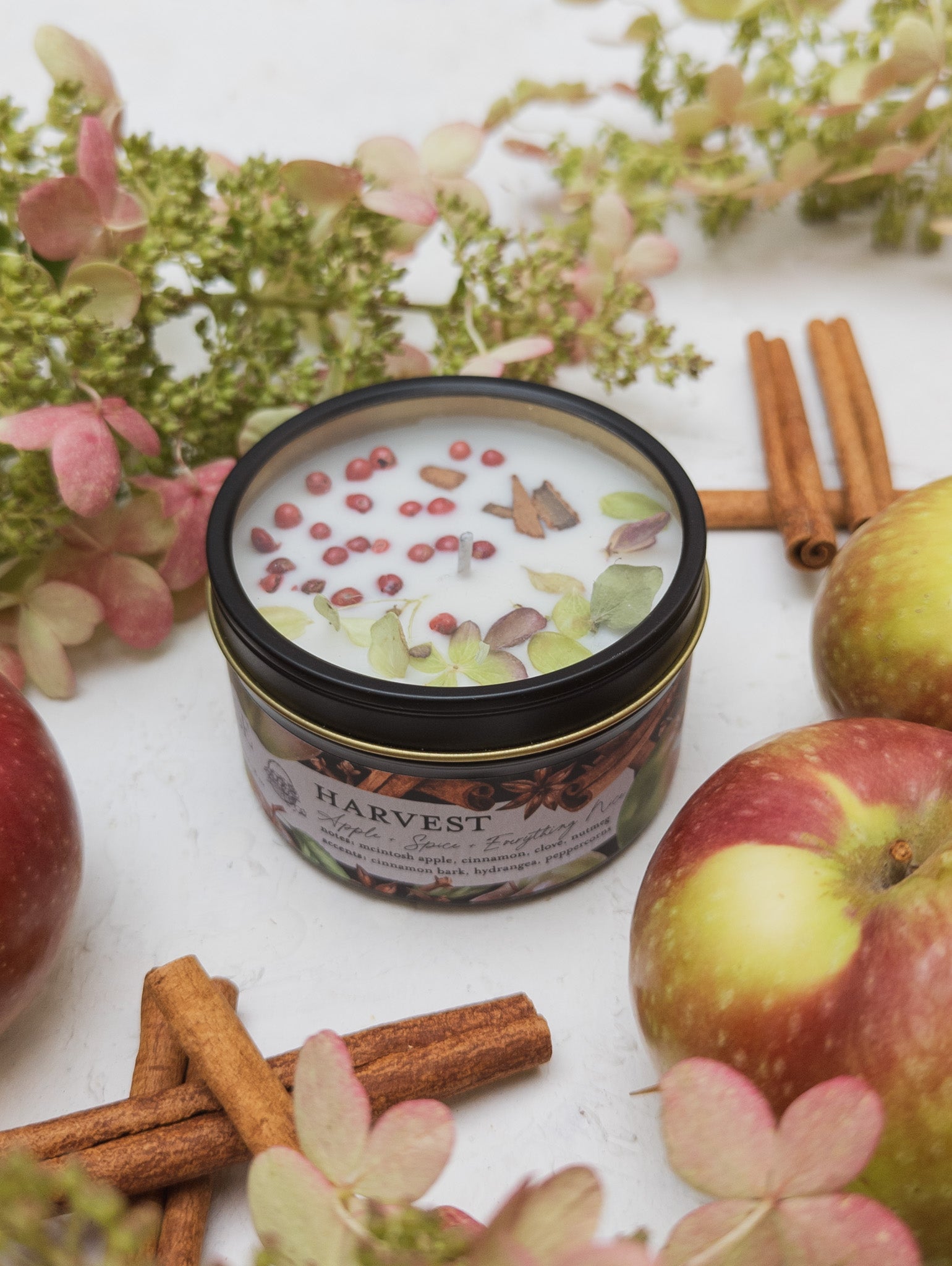 Harvest-themed candle with apples, cinnamon sticks, and flowers on a white surface