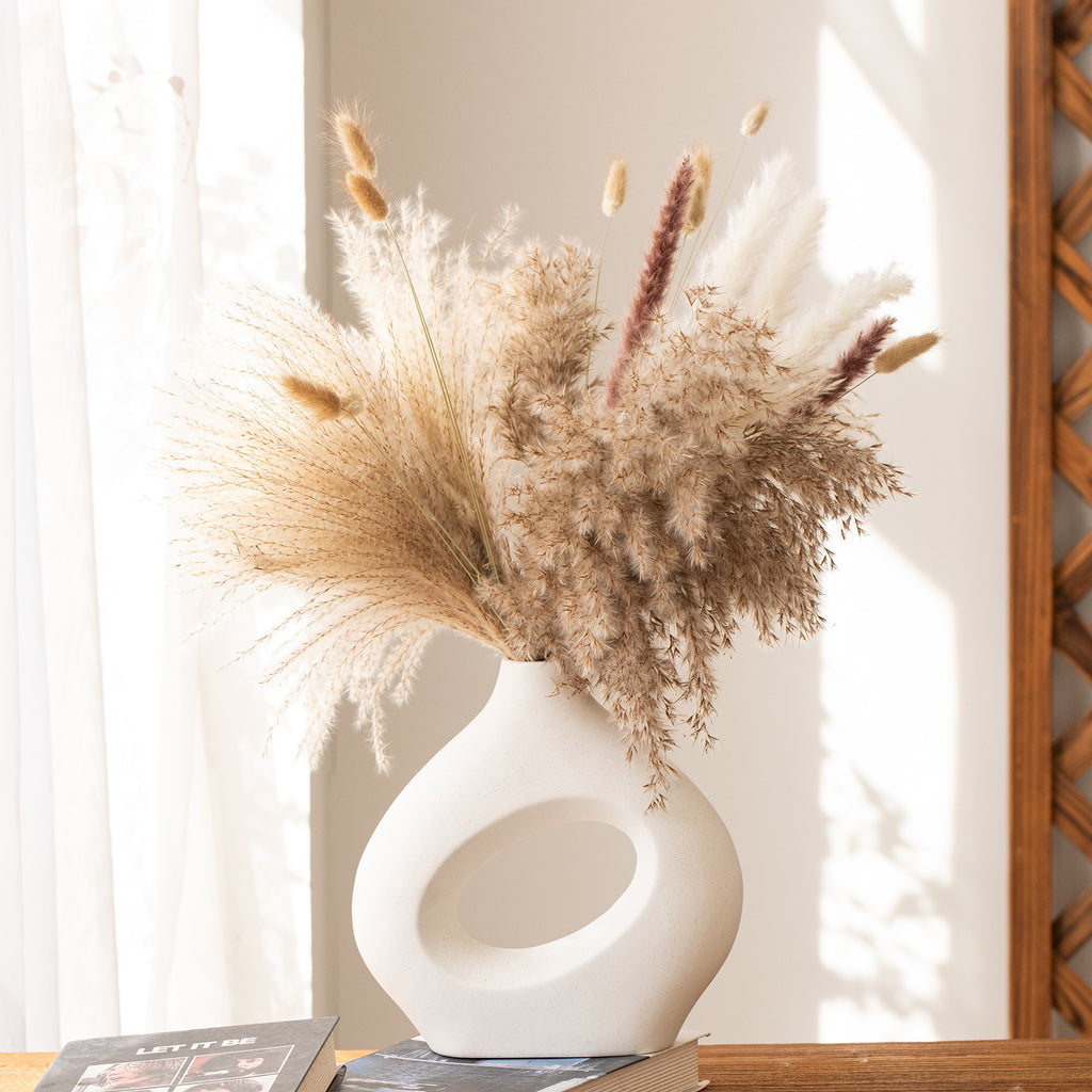 White vase with dried pampas grass on a wooden surface with a light background