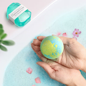 Hand holding a colorful bath bomb with a box labeled 'Diamond Soap' in the background.