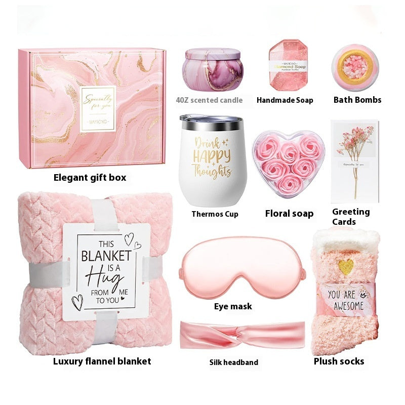 Collection of self-care products including a gift box, candle, soap, bath bombs, thermos cup, floral soap, greeting cards, blanket, eye mask, headband, and socks on a white background.